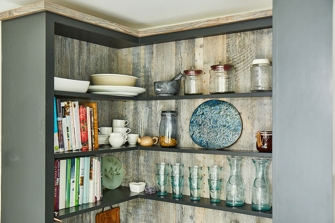 Glasses, mugs and books sit on tall bespoke open unit painted black with whitewash reclaimed wood backboards