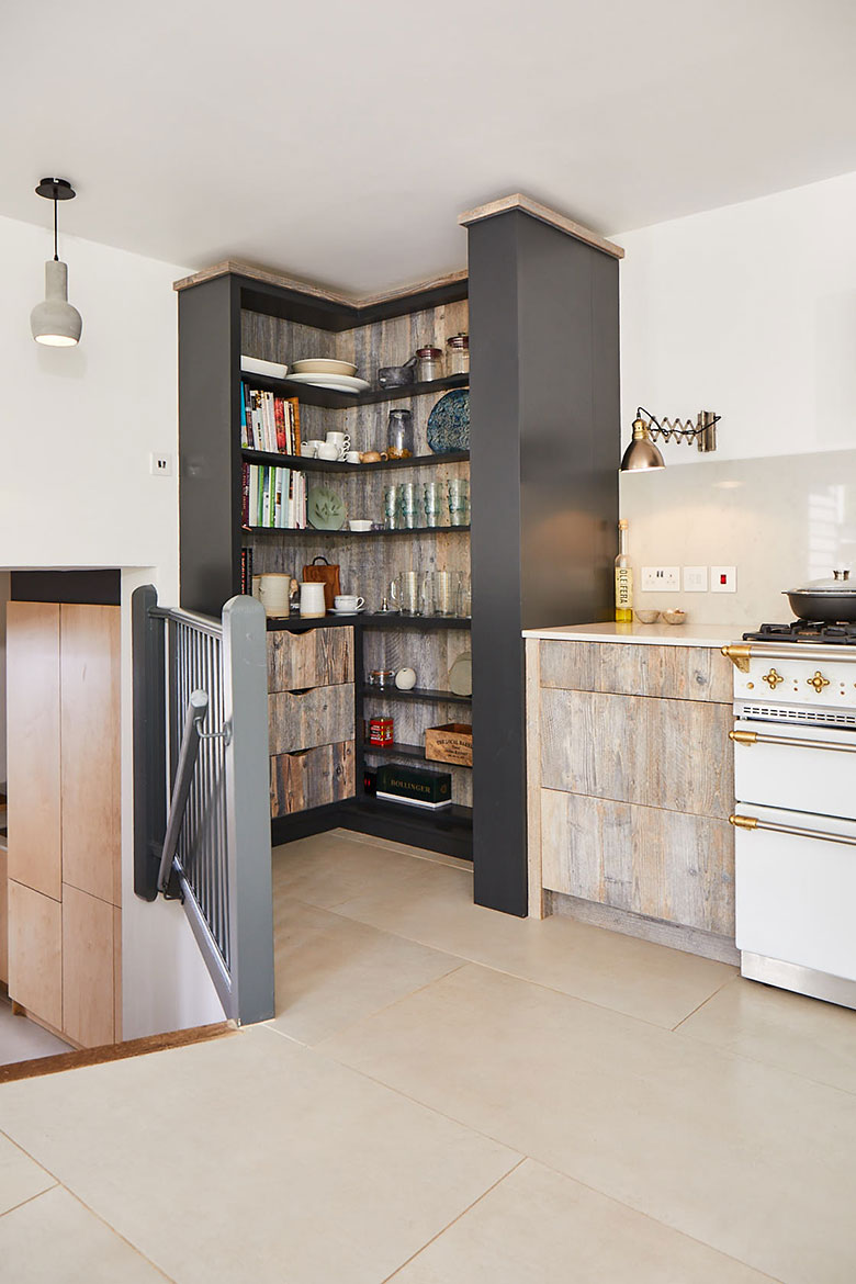 Tall open kitchen unit storing books glasses and mugs