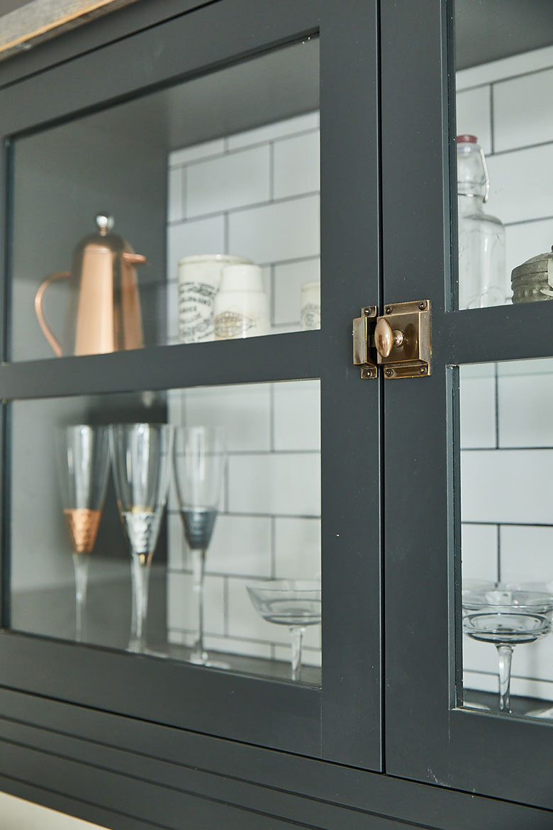 Bespoke kitchen wall cabinet painted lamp black with metro tiles behind and antique brass lock catch