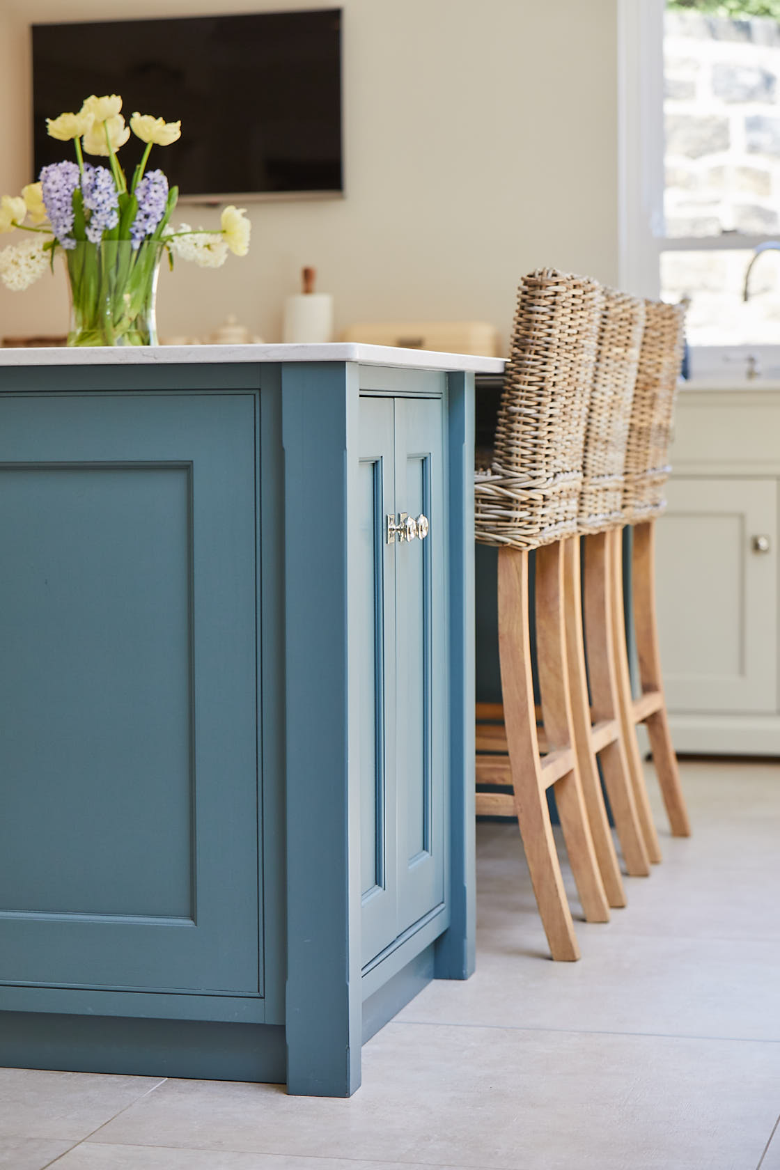 Flowers sit on painted kitchen island with wicker bar stools tucked under