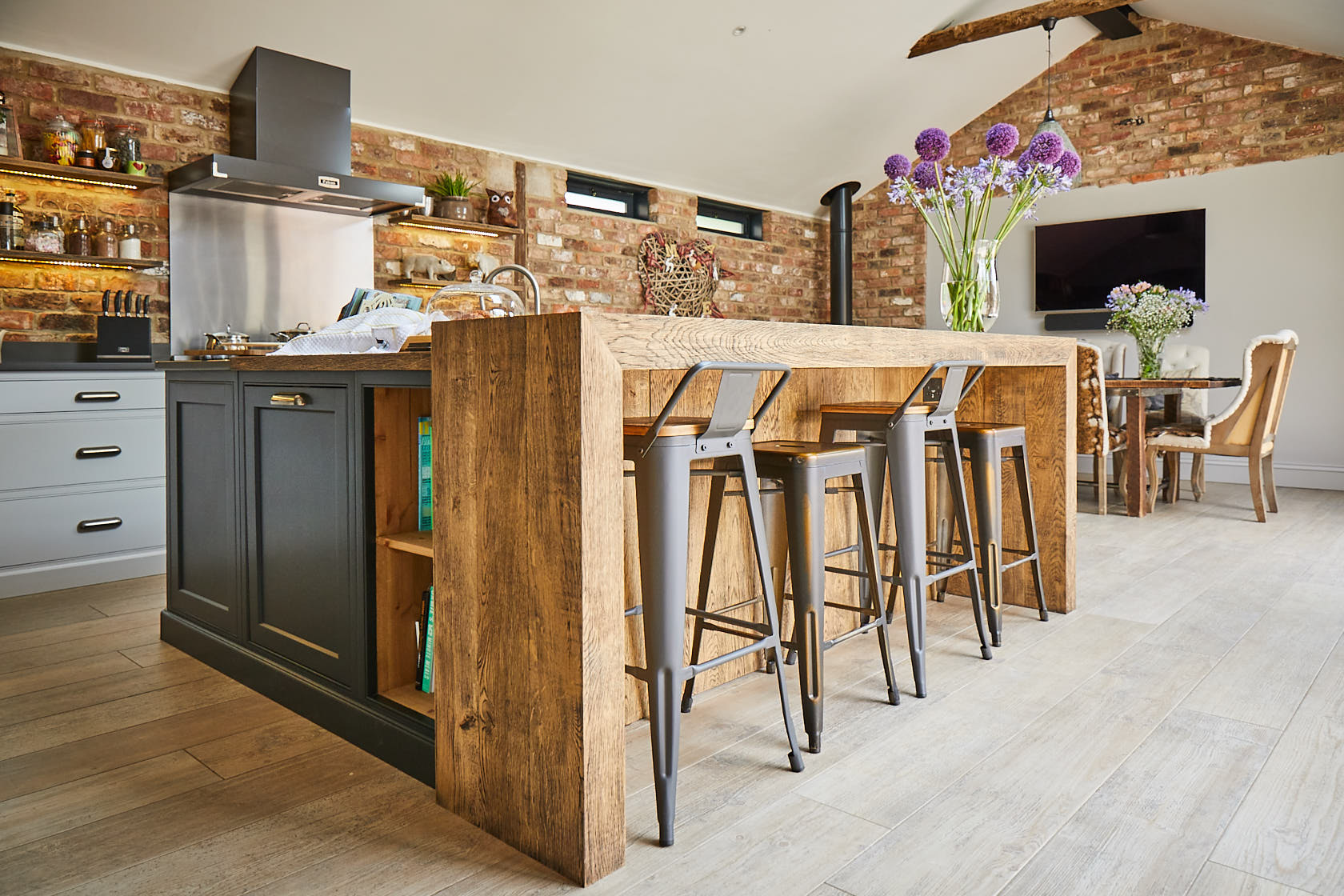 Open unit next to oak chunky breakfast bar and industrial metal bar stools