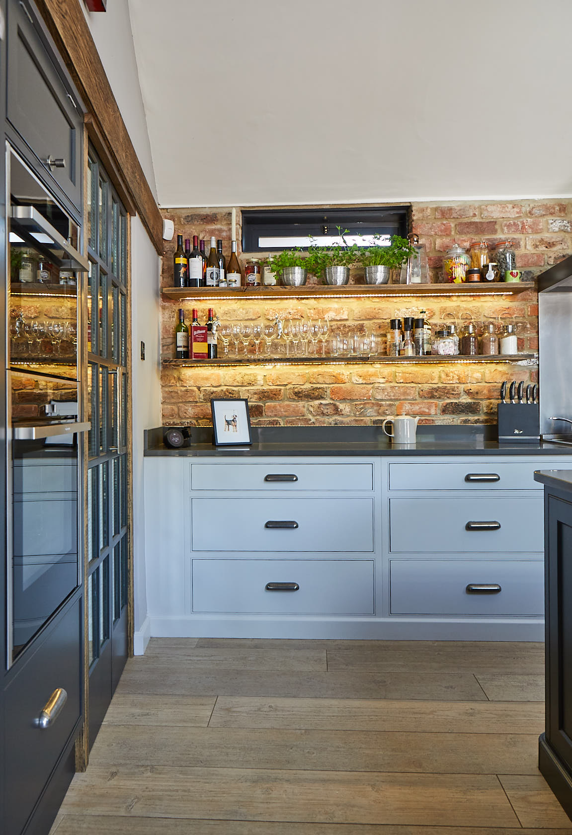 Light grey pan drawers below exposed brick wall with open rustic oak shelves above