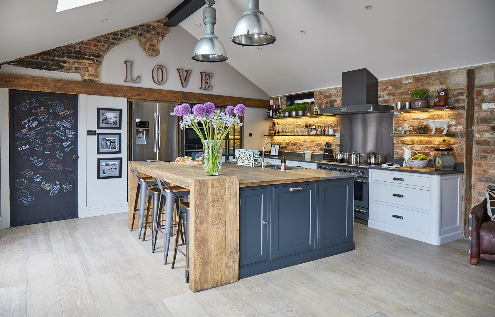 Flowers sit on large bespoke kitchen island with rustic oak breakfast bar and lamp black painted cabinets