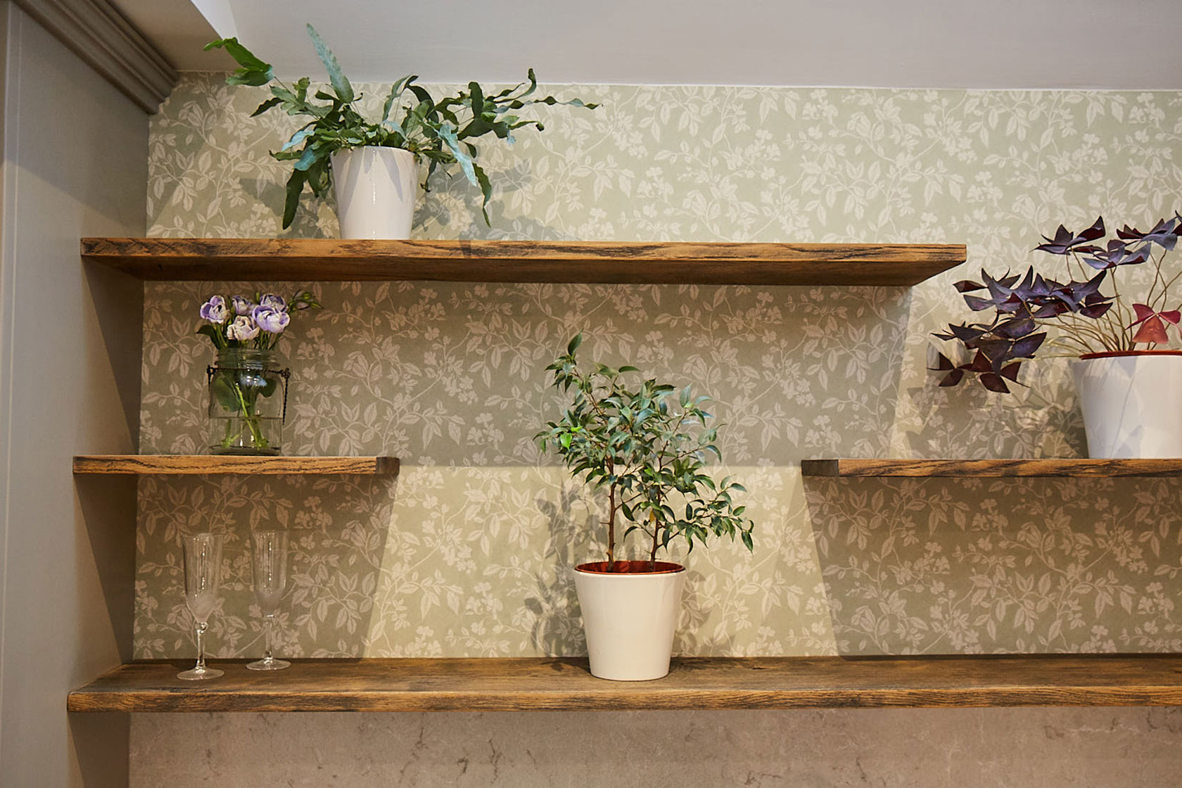 Plants sat on floating oak wood shelves with green floral back drop