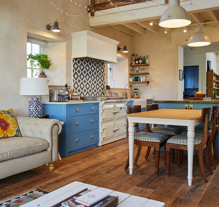 Open plan light blue kitchen with farmhouse table and cream sofa