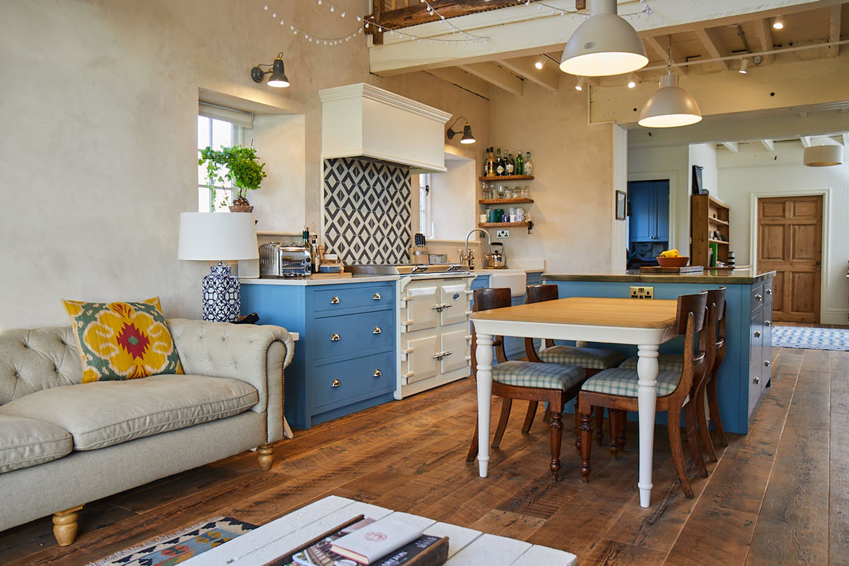 Open plan light blue kitchen with farmhouse table and cream sofa