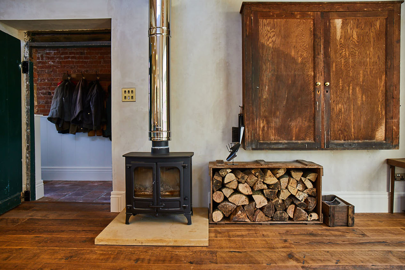 Rustic log burner sits on reclaimed floorboards with logs in log basket
