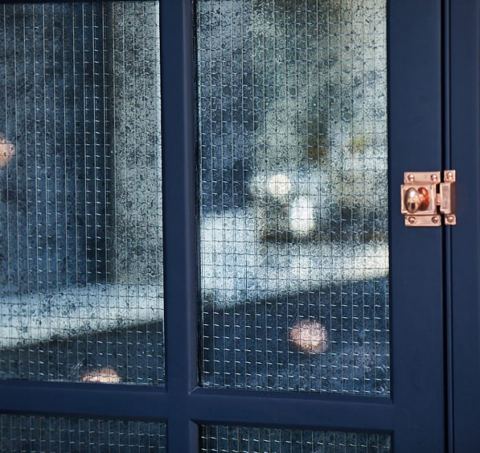 Mirror with wirework reflects dark blue kitchen