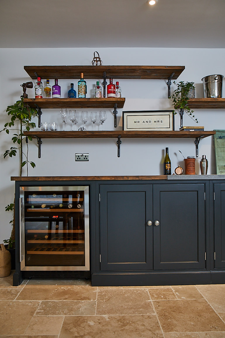 Wine cooler sits below open rustic shelves with plants and books