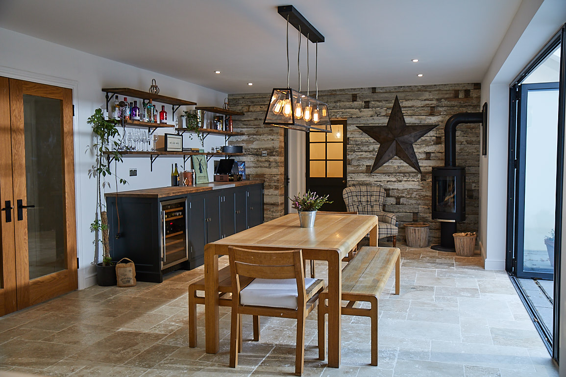 Oak dining table and bench sits in open plan kitchen with cladded wood wall