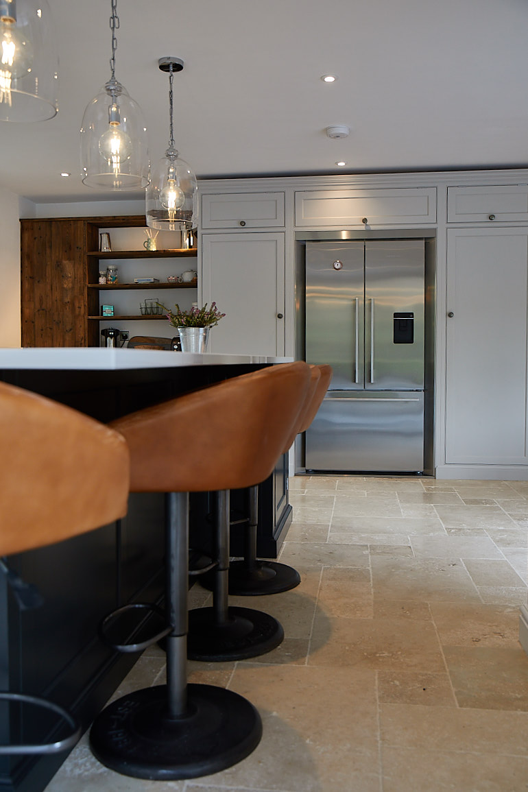 Light leather bar stools sit in front of Fisher & Paykel American fridge freezer integrated in painted kitchen units