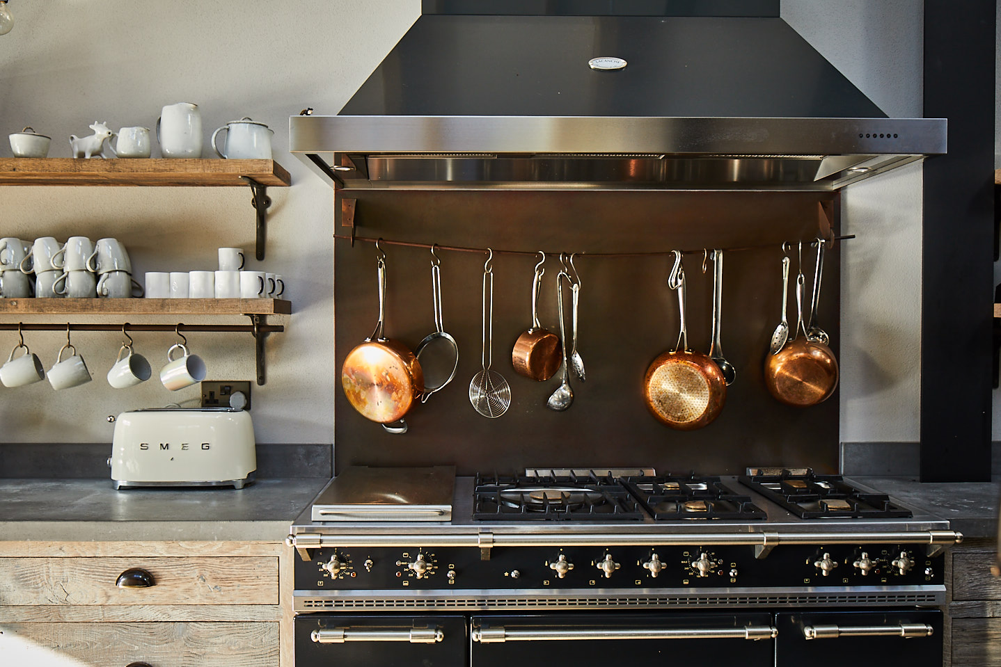 Copper pans hanging above range cooker with large industrial stainless steel extraction