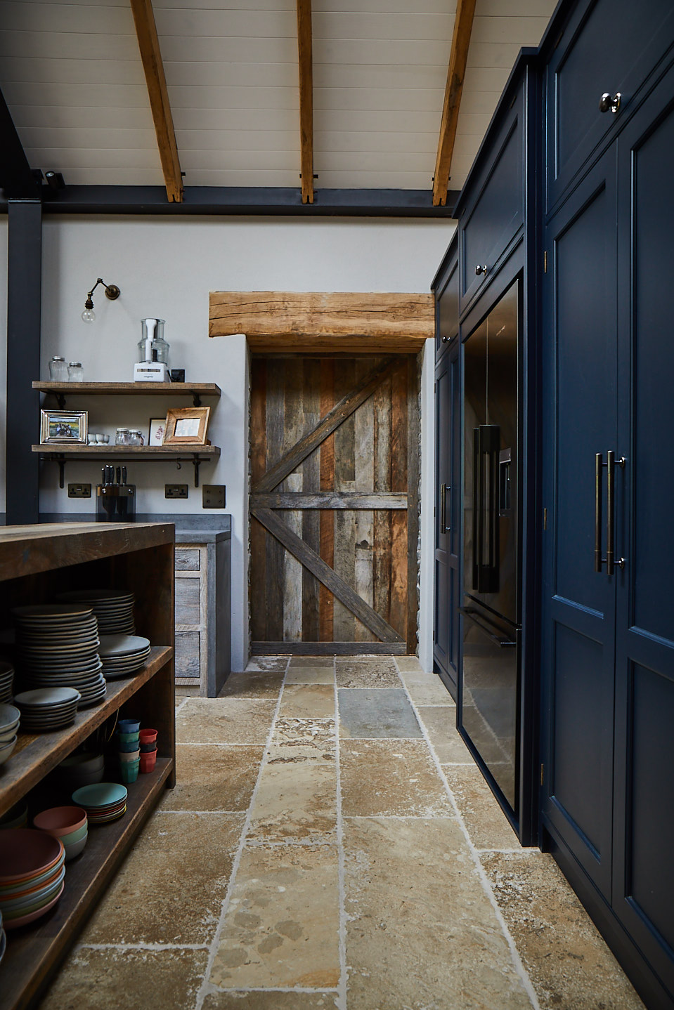 Reclaimed oak sliding barn door next to tall painted dark blue kitchen cabinets