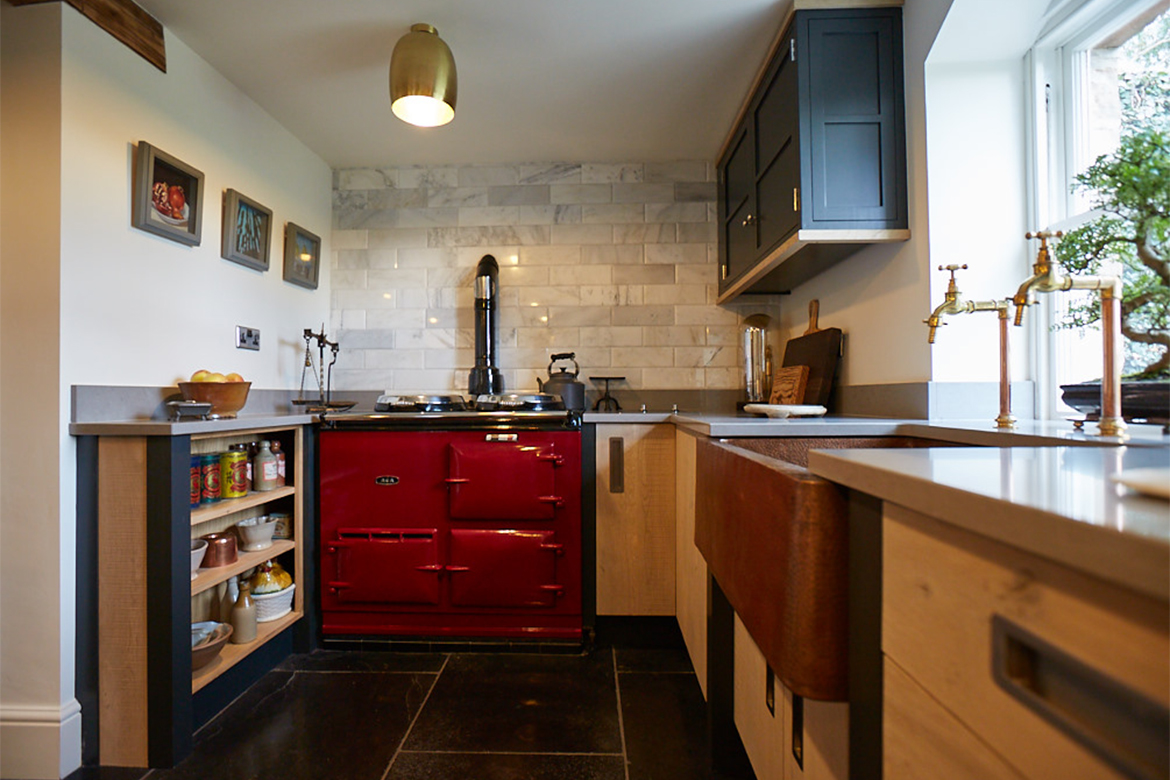 Red AGA sits between bespoke engineered kitchen cabinets and dark painted posts