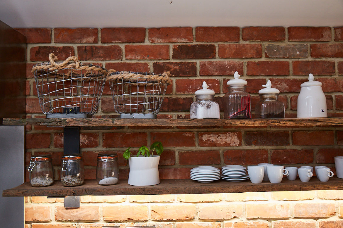 Bespoke reclaimed open oak shelving against an exposed brick wall with various accessories including plates, wirework and vessels