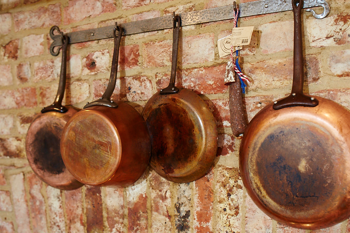 Copper pans hanging against exposed brick wall