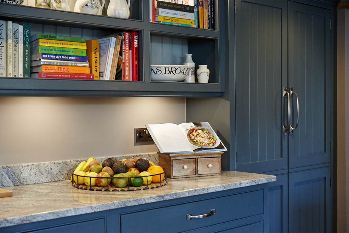 Fruit bowl sits on top of granite work surface with bespoke open book case above
