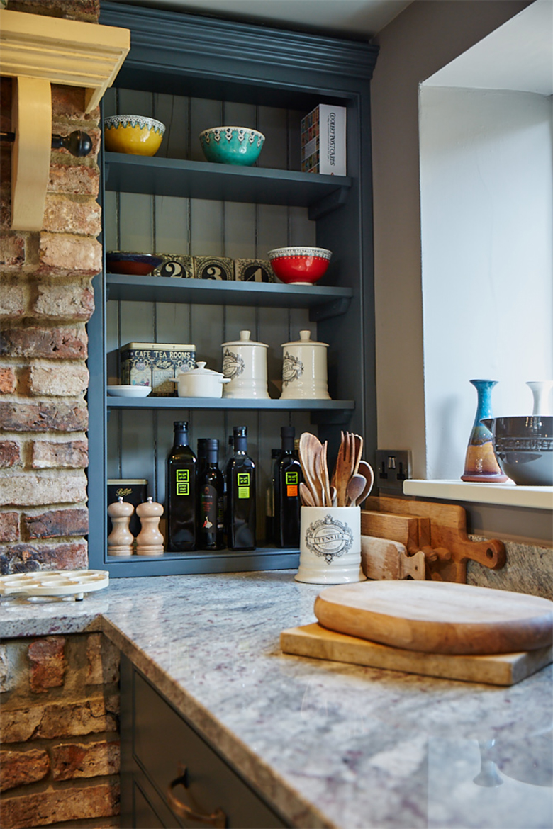 Bespoke kitchen unit scribed to exposed brick wall filled with bowls and oils