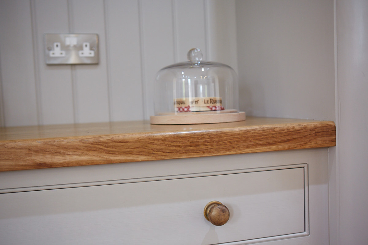 Glass cake cover sits on top of painted kitchen cabinets with solid oak worktop