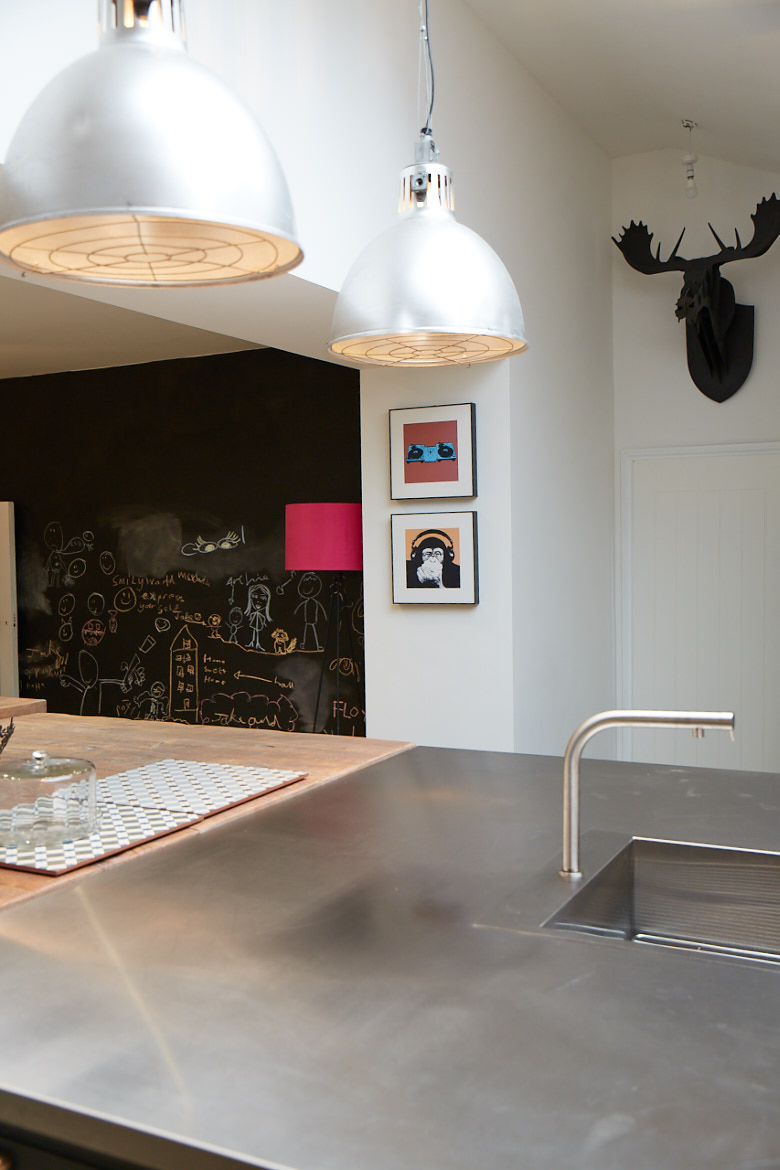 Bespoke stainless steel kitchen island worktop with large stainless pendant lighting above and black stag in background
