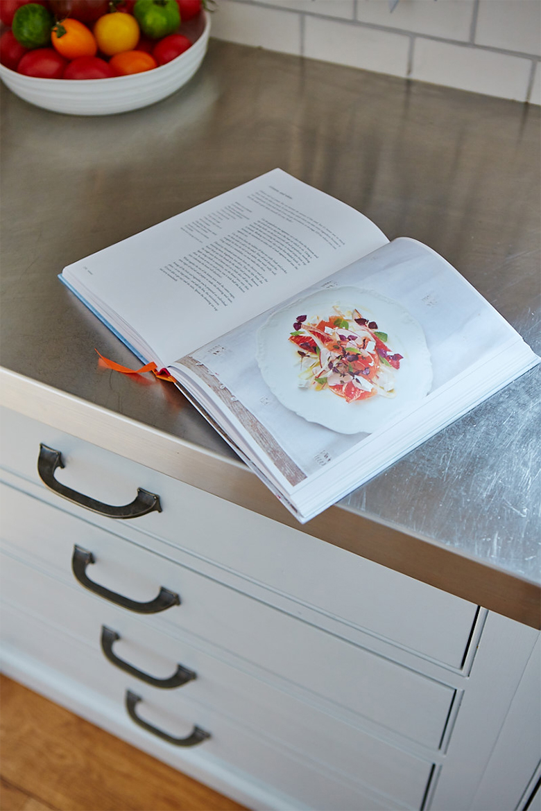 Book open on stainless steel worktop and bespoke painted drawer cabinet with pewter pull handles