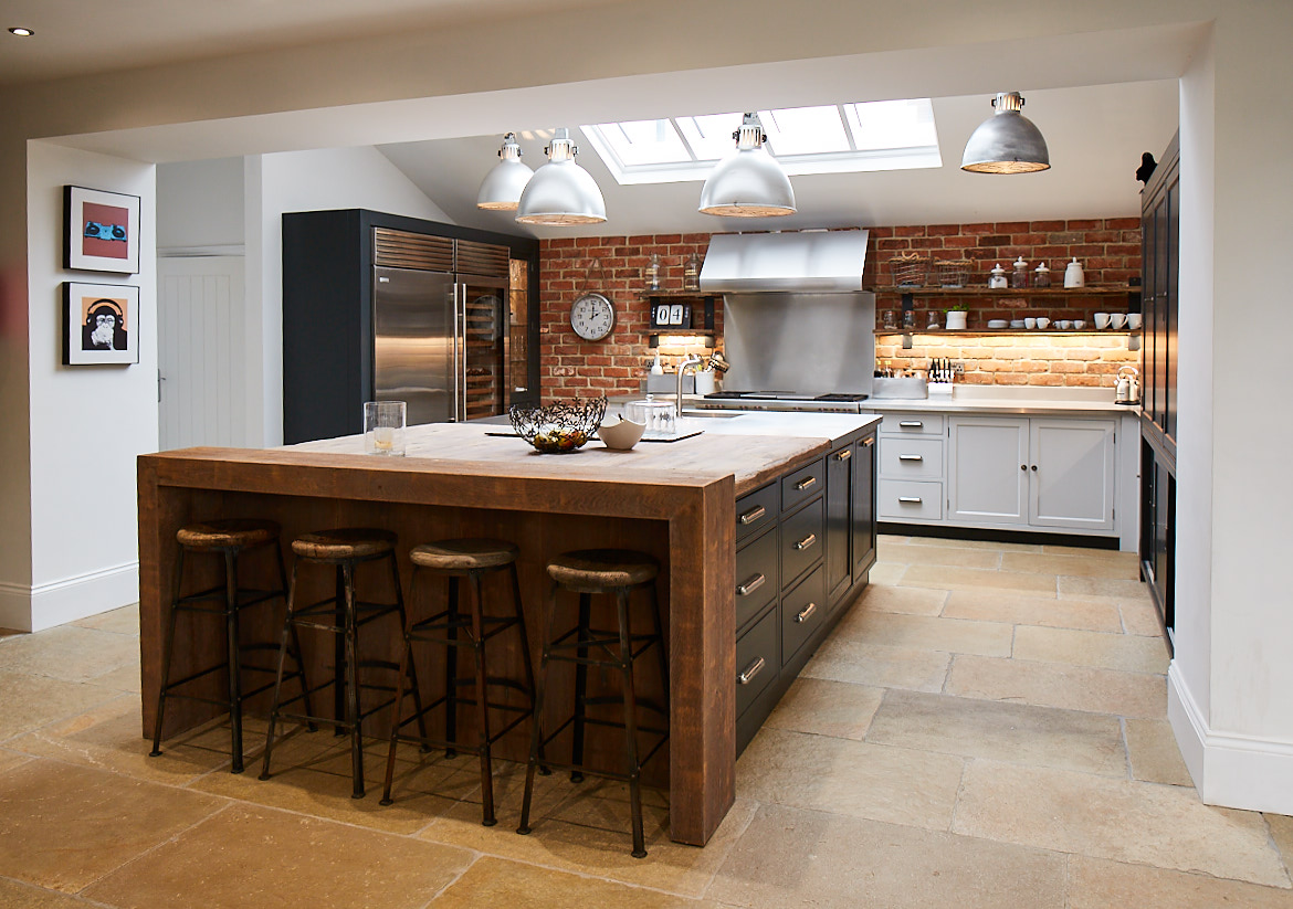 Wide shot of full kitchen by The Main Company including exposed brick wall bespoke painted island and reclaimed oak breakfast bar with complementing stools