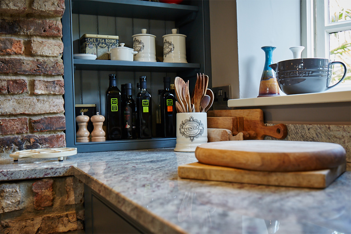 Chopping boards sat on granite in front of open bespoke wall unit with tongue and groove back panel