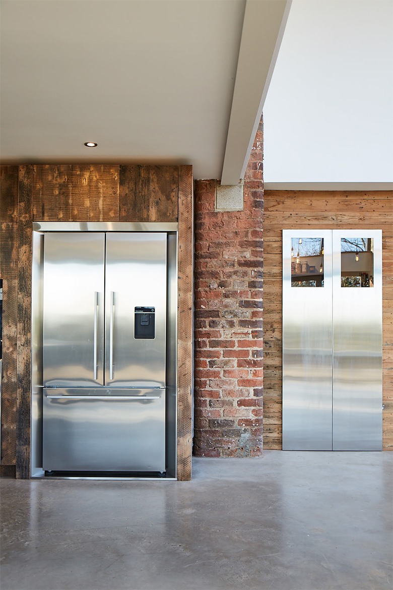 Stainless steel American fridge freezer with fisher paykel surround sits beside bespoke kitchen stainless steel pantry doors