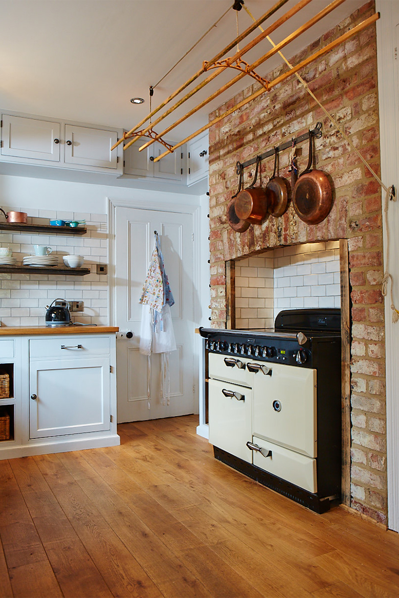 Cream range cooker in exposed brick chimney breast and hanging copper pans