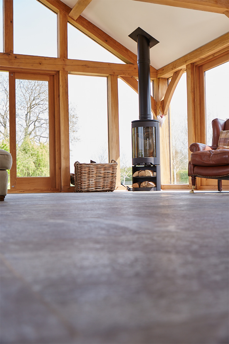 Open log burner sits on grey stone tile floor in oak beam house