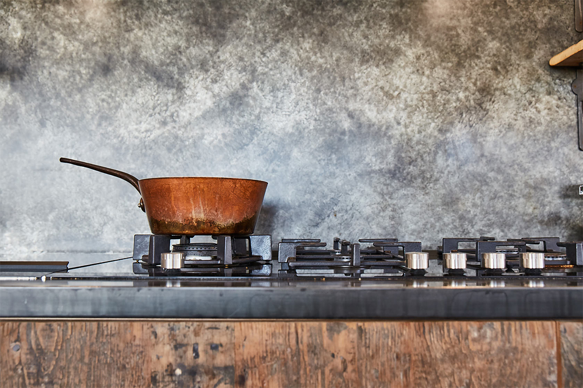 Copper pan sits on bespoke kitchen units with zinc patina worktop and matching backsplash