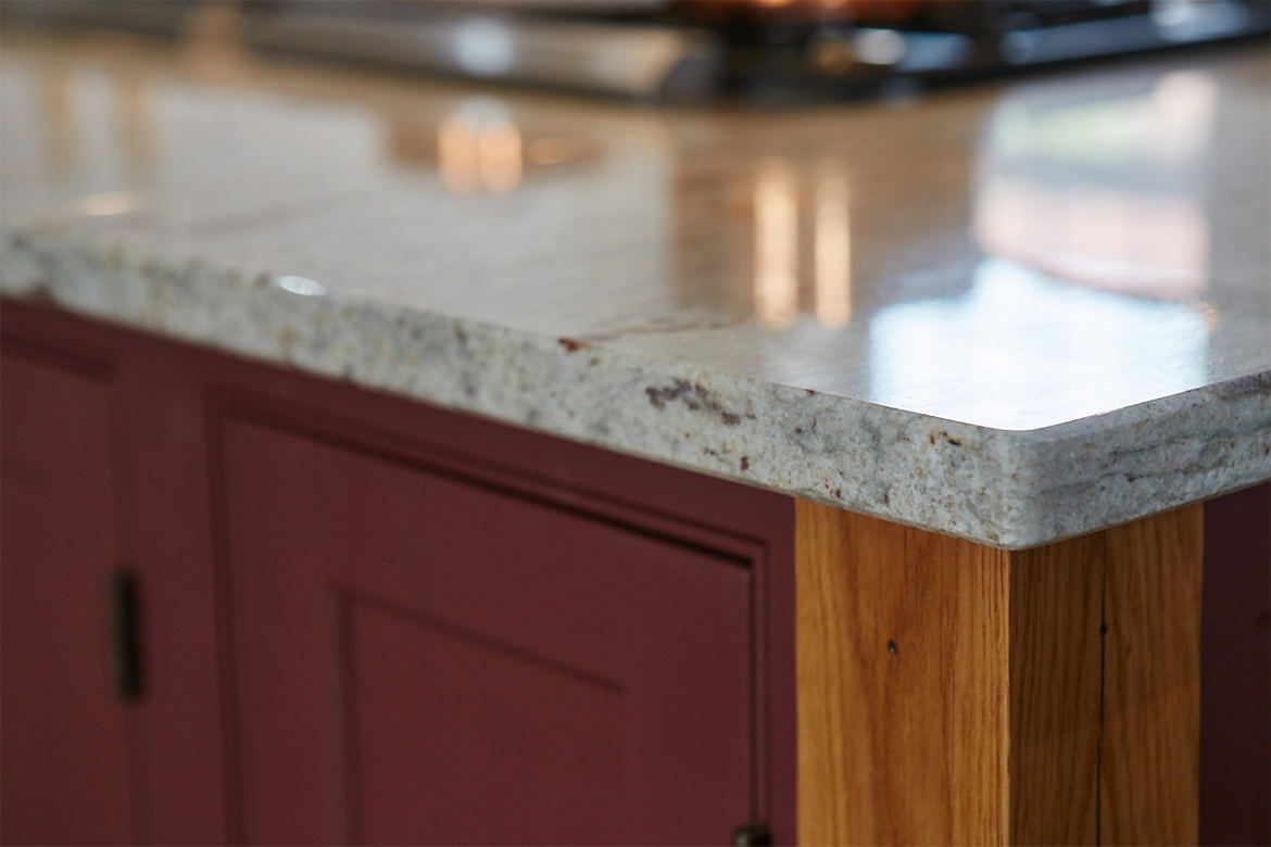Close up of granite, oak leg and painted plum colour of kitchen cabinets