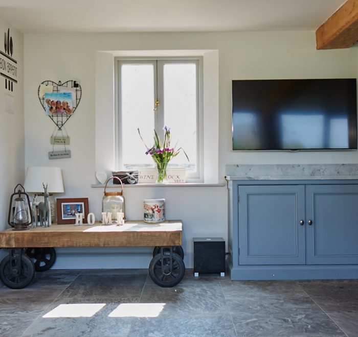 Reclaimed oak wood cart sits in front of window with traditional painted bespoke kitchen cabinets