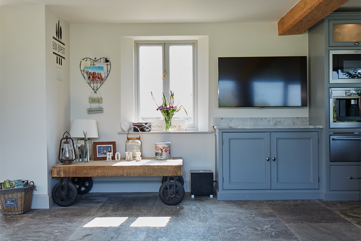 Reclaimed oak wood cart sits in front of window with traditional painted bespoke kitchen cabinets