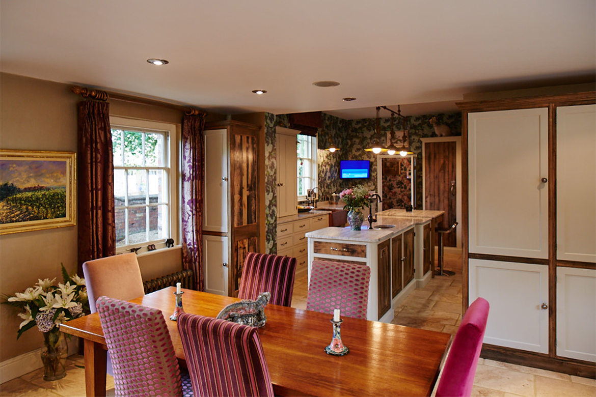 Dining table with upholstered chairs sits alongside vibrant bespoke kitchen