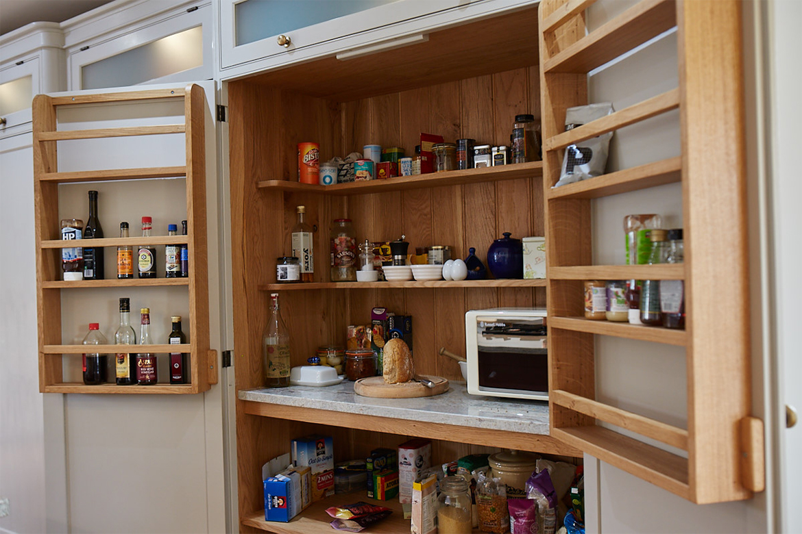 Internals of solid oak larder with freestanding microwave sat on granite and oak shelves full with food