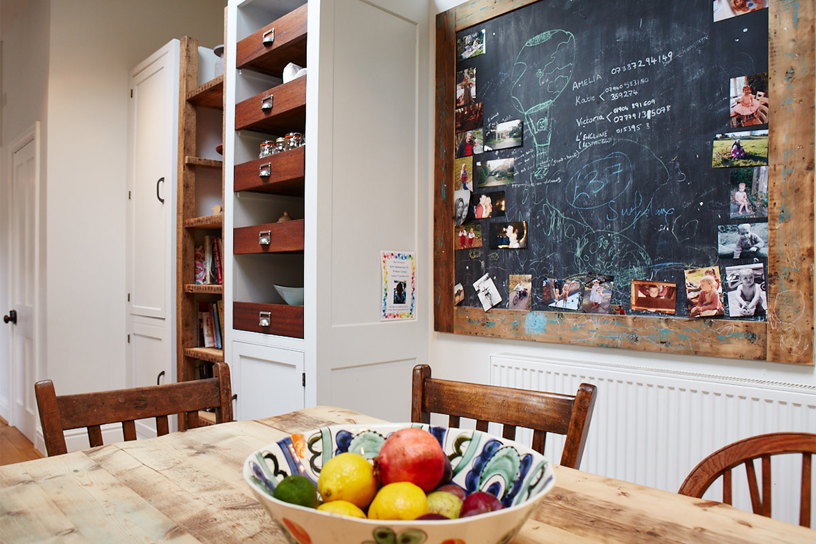 Tall bespoke kitchen cabinets with blackboard and fresh fruit on reclaimed wood table