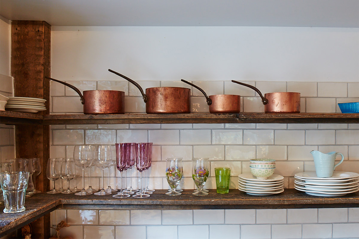 Reclaimed oak shelves against white metro tiles with copper pans