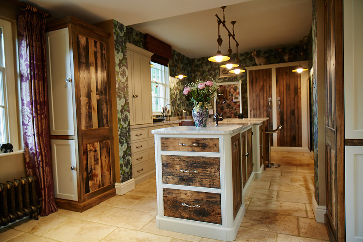 Reclaimed and painted bespoke kitchens cabinets sat on light stone floor with reclaimed oak drawer fronts in foreground