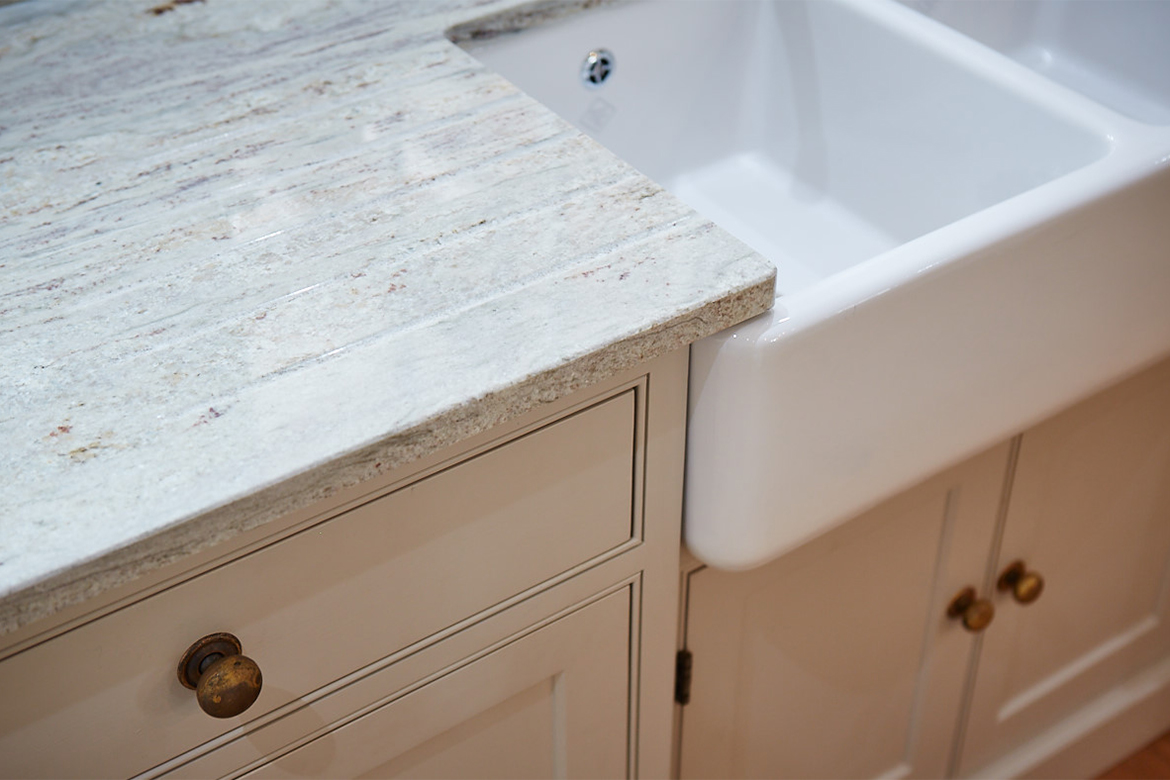 Close up detail of shaws double belfast sink with granite worktops and painted kitchen cabinets with burnt brass knobs
