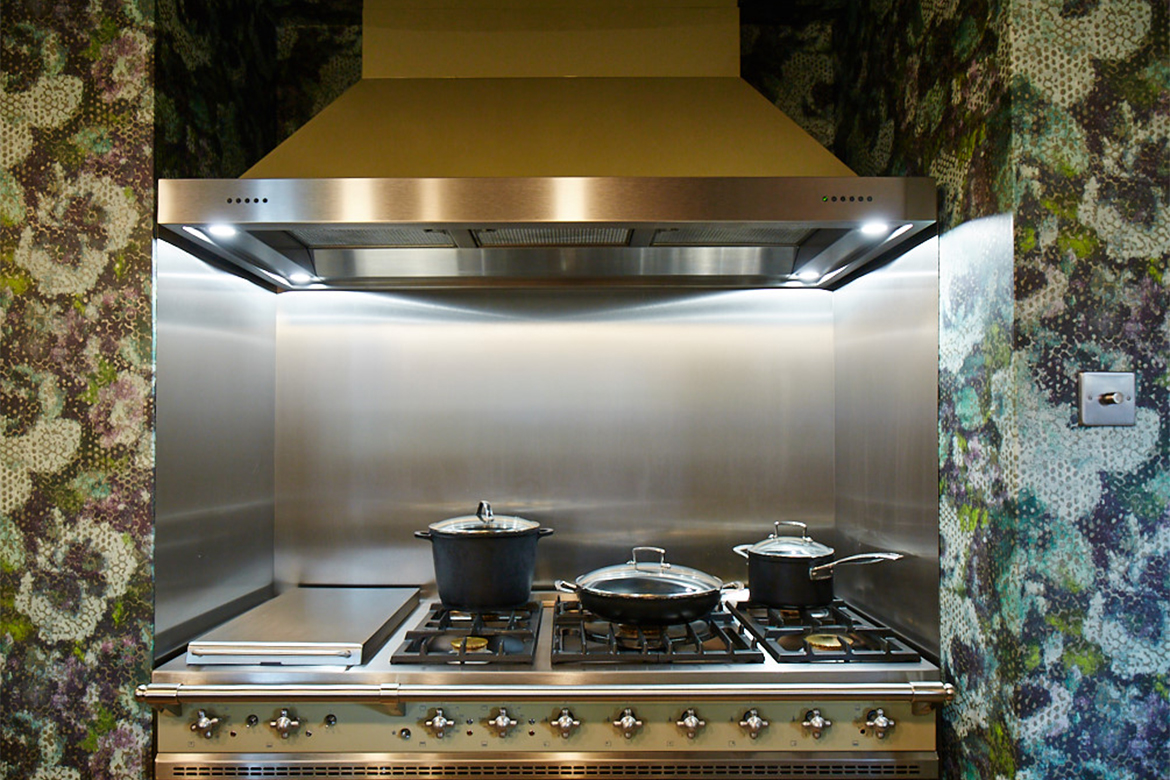 Green Chaussin Lacanche range cooker sat in alcove with colourful wall paper and stainless steel backsplash