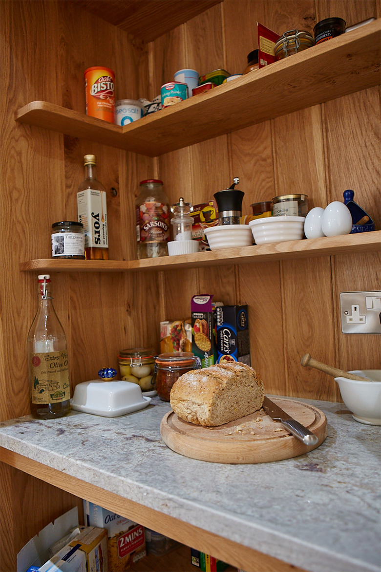 Bread and food being prepared inside bespoke oak larder cupboard with granite worktop and wrap around shelves
