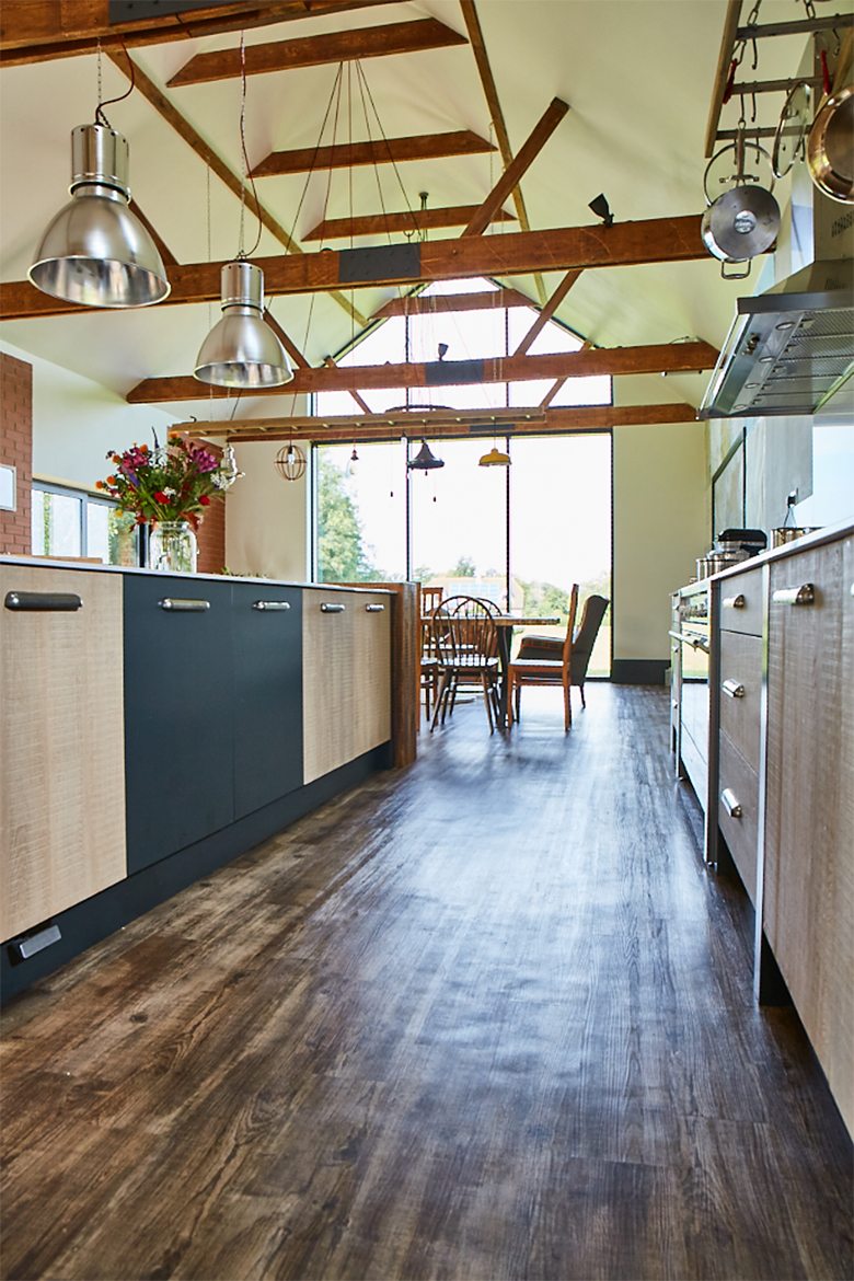 Reclaimed wood kitchen floor below high vaulted ceiling with exposed wood beams