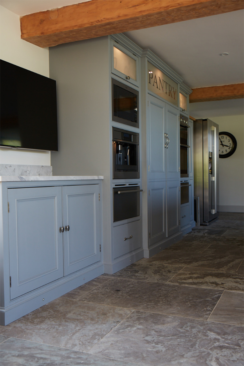 Tall bespoke kitchen units house integrated appliances with grey stone floor