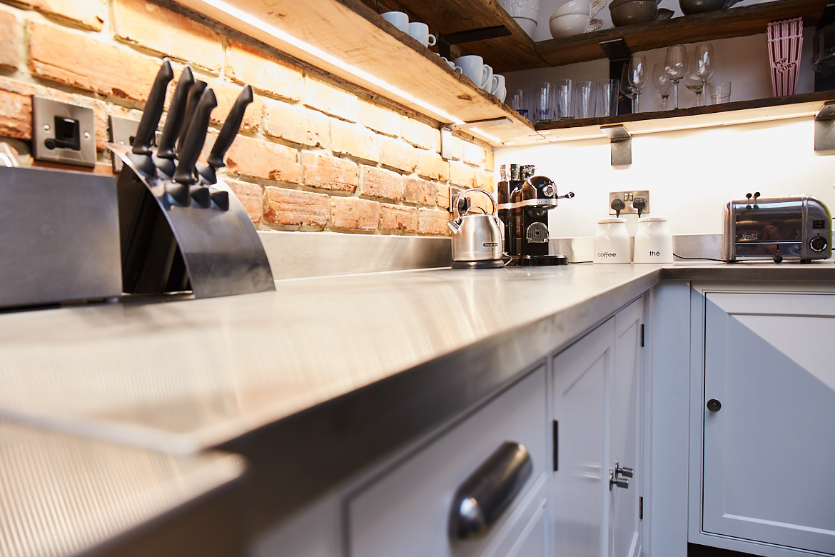 Close up of bespoke stainless steel worktop with knife block in background and finesse pewter handle