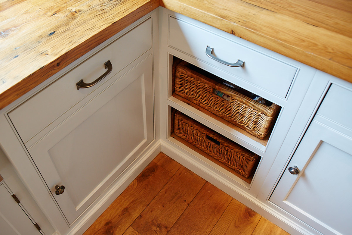 Bespoke painted corner unit with exposed wicker baskets reclaimed pine worktop and pewter pull handles