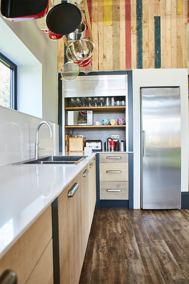 Pans hang over sink off reclaimed ladder in front of stainless steel tambour door