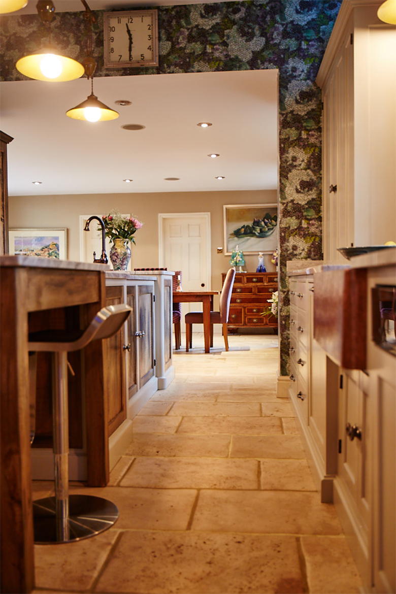 Light stone kitchen tiles with floral green wallpaper and bespoke kitchen