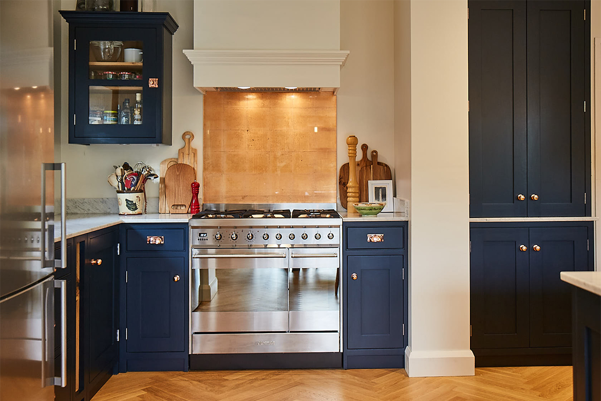 Freestanding range cooker with copper splash back and pained white extraction surrounded by low blue pained kitchen units