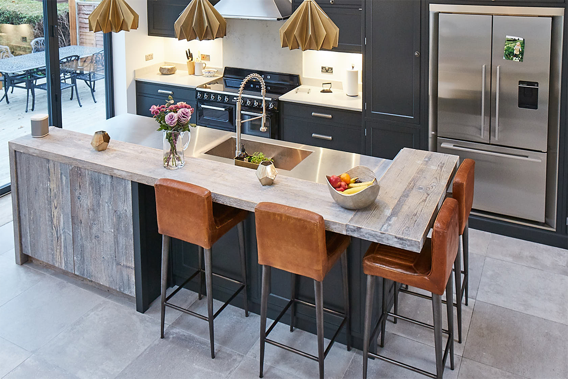 Large kitchen island with grey tiled floor and painted black units with contrasting stainless steel worktop